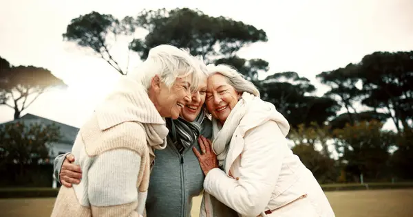 Talking, laughing and elderly woman friends outdoor in a park together for bonding during retirement. Happy, smile and funny with a group of senior people hugging in a garden for humor or fun.
