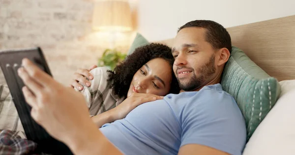 Couple, tablet and scroll in bed, morning and bond with internet video, movie and meme for love, care and hug. Man, woman and digital touchscreen for typing, social network app or web blog in house.