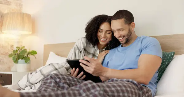 Couple, tablet and laughing in bed, morning and bond with funny video, movie or meme for love, care or hug. Man, woman and digital touchscreen for typing, comic social network or online game in house.