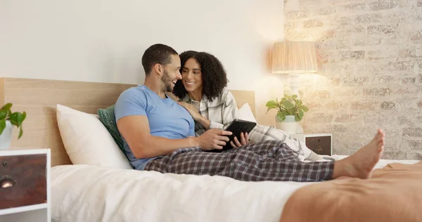 Couple, tablet and relax in home bedroom, laugh or morning with video, movie or meme for love, care or hug. Man, woman and digital touchscreen for typing, social network app or bond together in house.