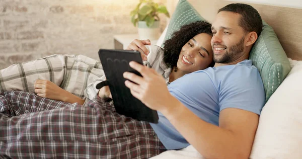 Couple, tablet and scroll in bed, morning and bond with internet video, movie and meme for love, care and hug. Man, woman and digital touchscreen for typing, social network app or web blog in house.