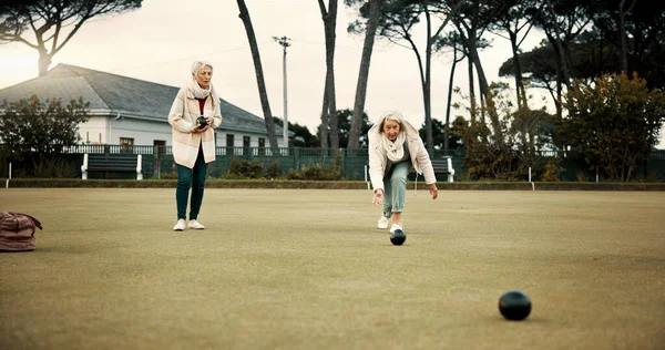 Women, park or old people bowling for fitness, training or exercise for wellness or teamwork outdoors. Senior ladies, relax or elderly friends playing fun ball game or sport in workout together.