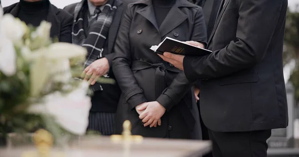 Bible, hands and family at funeral, cemetery or burial ceremony religion by coffin tomb. Holy book, death and grief of people at graveyard, Christian priest reading spiritual gospel and faith in God.