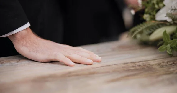 Death, funeral and hand of man on coffin, family at service in graveyard or church for respect. Flowers, loss and people at wood casket in cemetery with memory, grief and sadness at grave for burial