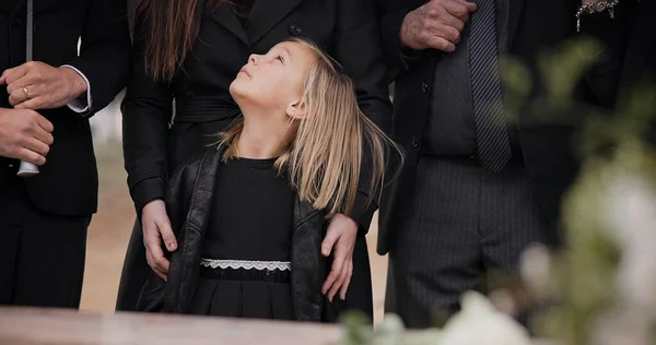 Mourning, grief and family with girl at funeral, flowers on coffin, death and sad child at service in graveyard. Support, loss and people at casket in cemetery with kid crying at grave for burial