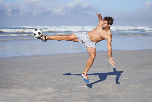 stock image Man, beach and kicking soccer ball for game, sports or exercise in outdoor hobby, training or practice. Young muscular male person or football player in match or cardio workout by ocean coast or sea.