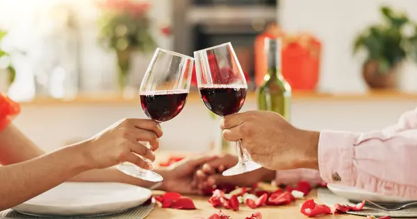 Couple, hands and toast with wine glass for home celebration of love, romance and valentines day on anniversary. People, table and date success with red champagne, drinks or luxury dinner with roses.