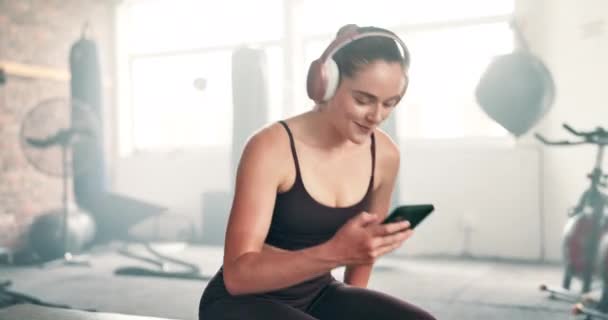 快乐的女人 耳机和电话在健身房休息 为音乐 播客或社交媒体 年轻女性或运动员在健康俱乐部的手机上休息 放松或听声音 — 图库视频影像
