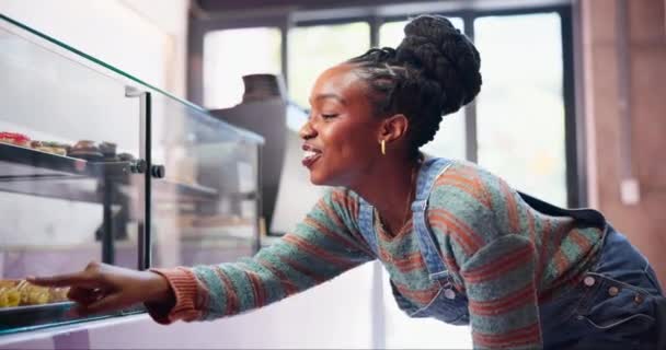 ベーカリー カウンター 黒人女性は お菓子を扱う中小企業で幸せな顧客のためのペストリーを選択します ディスプレイウィンドウのカフェ スイーツ ガラスのケーキ デザート クッキーの決定 — ストック動画