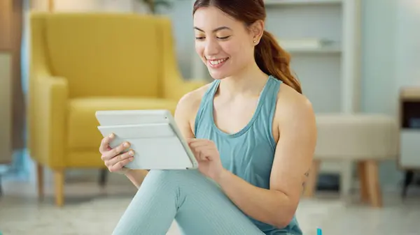 Fitness, internet and woman streaming on a tablet for training, yoga and exercise on the floor of her house. Happy, young and wellness girl with technology for a workout, cardio or video on pilates.