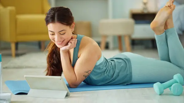 Fitness, internet and woman streaming on a tablet for training, yoga and exercise on the floor of her house. Happy, young and wellness girl with technology for a workout, cardio or video on pilates.