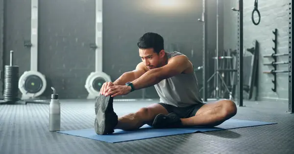 Man, break and stretching on gym floor in fitness, workout or training for strong muscles, heart health or cardio wellness. Japanese personal trainer, sports person or coach in body warmup exercise.