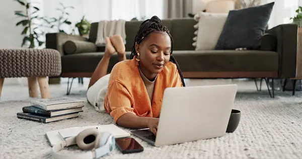 Laptop, education and a student black woman on the floor of a living room to study for a test or exam. Computer, smile and a happy young person learning with an online course for upskill development.