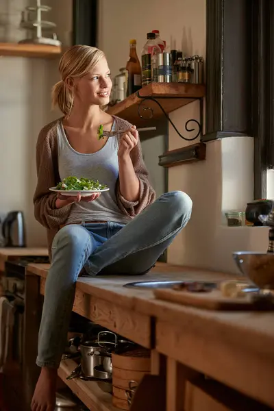 Thinking, woman and eating salad in home kitchen, nutrition and fresh leafy greens for healthy diet. Food, bowl and smile of hungry person with vegetables, lunch or organic vegan meal for wellness.