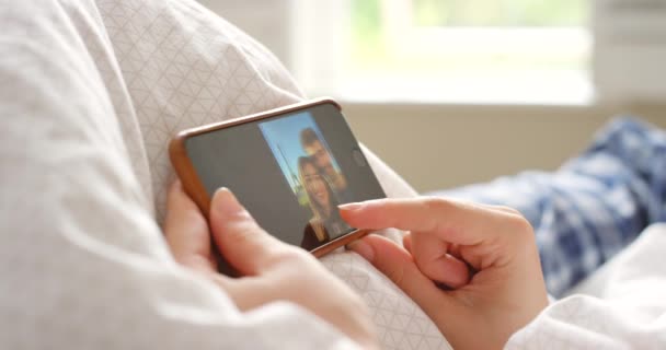 スクリーン カップルは 自宅のベッドでソーシャルメディアのために一緒に写真を見ています クローズアップの人々は アパートのベッドルームでリラックスして携帯電話のギャラリーで画像をスワイプ — ストック動画