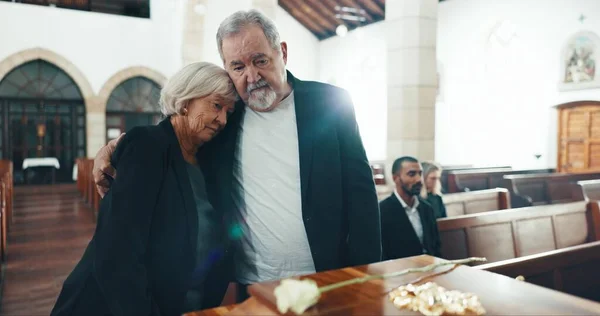 Funeral, coffin and senior couple hug in church for goodbye, mourning and grief in memorial service. Depression, sad family and man embrace woman by casket for greeting, loss and burial for death.