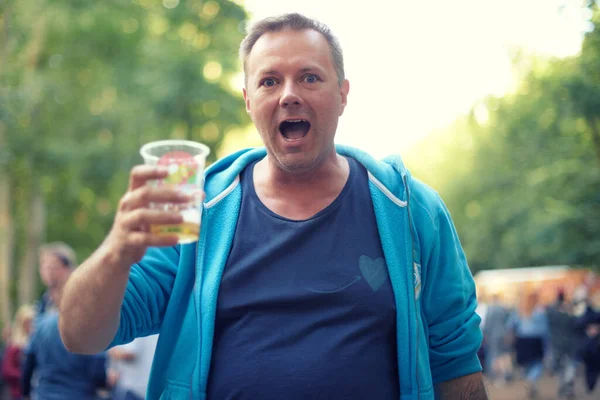 Mature, man and portrait with beer outdoor at festival in park, woods or party in nature. Person, drinking and toast with plastic cup with alcohol for celebration at event in forest or summer.