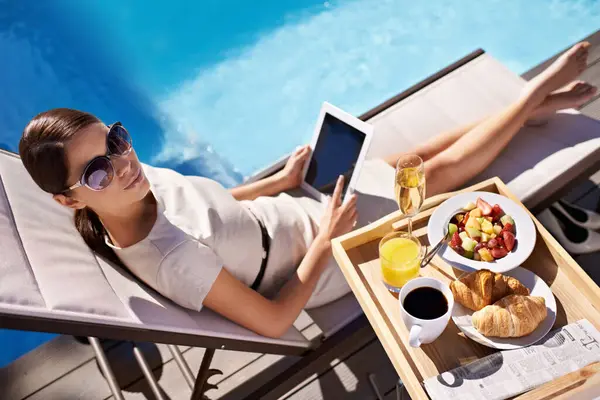 Hotel, pool and woman with breakfast, tablet and relax on business trip for food or drink service. Travel, hospitality and businesswoman on lounge chair at brunch with summer, luxury or villa holiday.