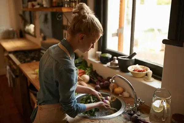 Woman in kitchen, cleaning vegetables and cooking, hygiene and health for food and nutrition at home. Chef skill, washing produce and catering, vegan or vegetarian meal prep with preparation.