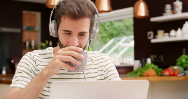 快乐的男人 笔记本电脑和耳机与咖啡在研究 社交媒体或沟通在家里 在网上聊天 发邮件或在厨房喝酒的男性或自由职业者的脸 — 图库视频影像