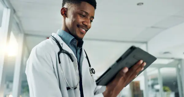 Tablet, research and happy black man doctor on internet for medical or healthcare information online in a hospital. Smile, medicine and professional typing on health website or app in a modern clinic.
