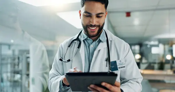Tablet, research and happy man doctor on internet for medical or healthcare information online in a hospital. Smile, medicine and professional typing on health website or app in a modern clinic.