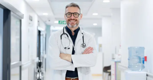 Professional, face and man or doctor with arms crossed for wellness, trust and service in hospital or clinic. Portrait, person and expert with happiness for career, cardiology or glasses at workplace.