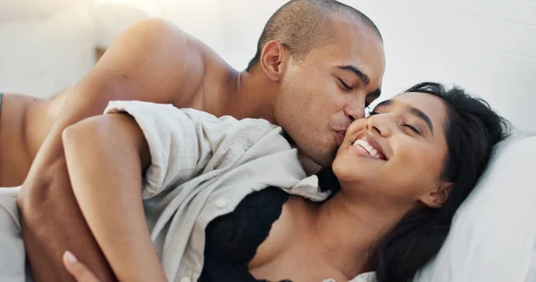 Happy couple, hug in bed and love with intimacy and romance at home for relationship, sex and bonding. Young people, woman and man relax in bedroom, cuddle and laughing with kiss and talking together.
