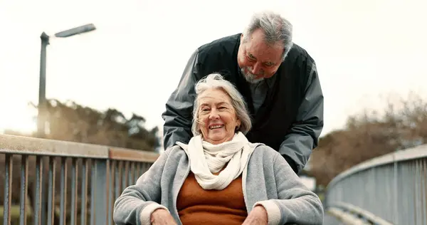 Senior couple, nature and in a wheelchair on a walk for happiness, retirement date or love. Smile, talking and an elderly man and woman with a disability and in a park to relax together in marriage.
