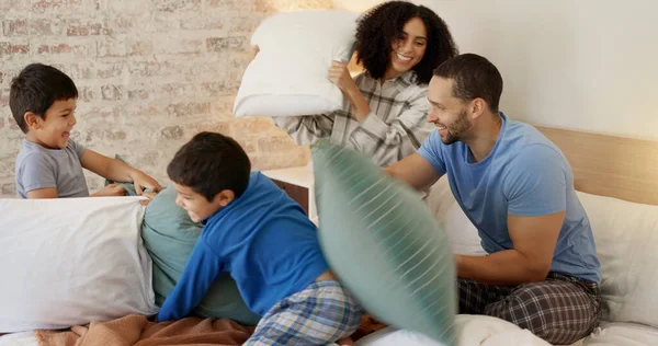 Happy family, pillow fight and bedroom with kids, playing and excited with love, bonding and care in home. Man, woman and boy children on bed for game, playful conflict or comic quality time in house.