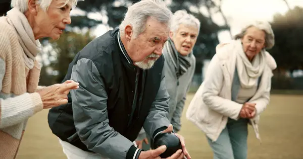 Senior man, game and senior people bowling in nature for retirement sports, teamwork and support. Bowling, friends and elderly man and woman in a group with a ball for a competition on a field togeth.
