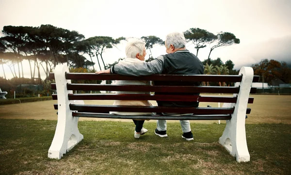 Hug, bench or old couple in park or nature talking or bonding together in retirement outdoors back view. Senior, elderly man or mature woman on date to relax with love, peace or care on calm holiday.