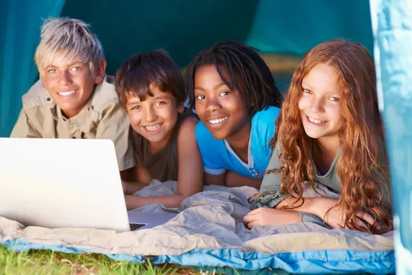 Children, portrait and happy with laptop for camping in tent, social media or online movie with diversity in nature. Friends, face and group with smile outdoor on grass for trip, relax or holiday fun.
