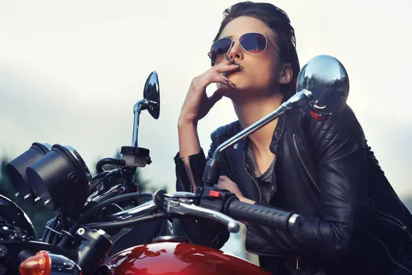 Bike, leather and woman smoking in city with sunglasses for travel, transport or road trip as rebel. Fashion, model and nicotine with attitude on classic or vintage bike for transportation or journey.