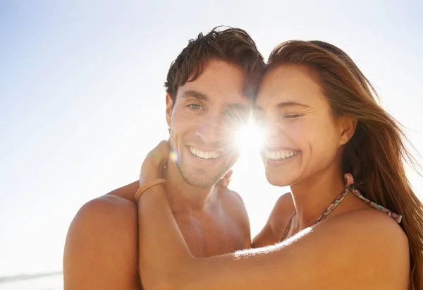 Love, laugh and couple hug at a beach with comic, humor or bonding, comedy or silly joke in nature. Face, flare and funny people embrace at sea with goofy moment on summer, holiday or travel vacation.