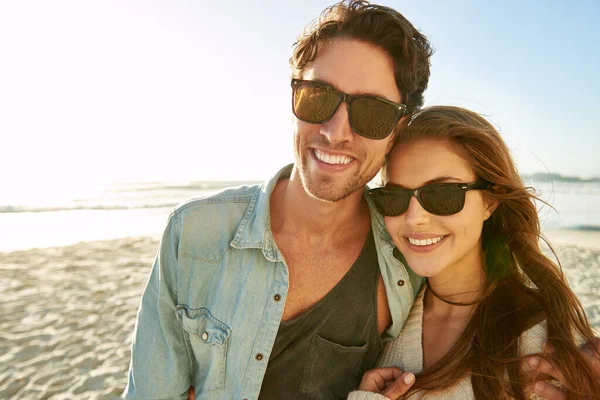 Couple, sea and sunglasses with embrace, smile or care for nature, eye protection or holiday in summer. Man, woman and hug with glasses at beach for sun, happy and love by ocean on tropical vacation.