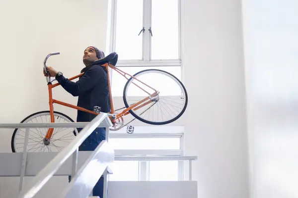 Bicycle, stairs and man carrying bike for exercise and eco friendly transportation with travel. Staircase, carbon neutral and cyclist with apartment complex and journey of walking steps in building.