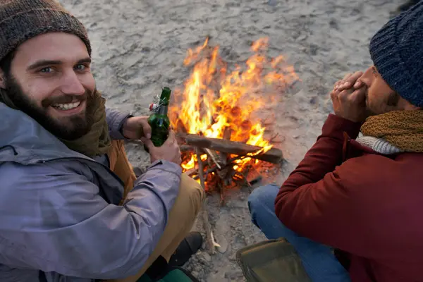 Campfire, friends and portrait with man and smile by the beach with vacation and camping. Ocean, outdoor and together with travel and people on a trip and journey with fire conversation by sea.