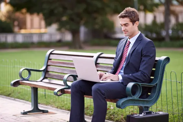 Businessman, laptop and typing on park bench in nature for trading, checking email or outdoor networking. Man or trader in business suit on computer for communication or finance on outside furniture.