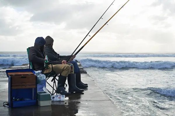 Ocean, fishing rod and men outdoor in winter, leisure activity at beach or harbor with friends in nature for seafood. Travel, seascape and waves with fisherman, recreation or hobby in the cold.