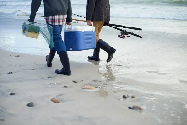 Closeup, walking and beach with fishermen, cooler box and activity with equipment or weekend break. People, ocean or friends with tools for hobby or early overcast morning with waves, sand or seaside.
