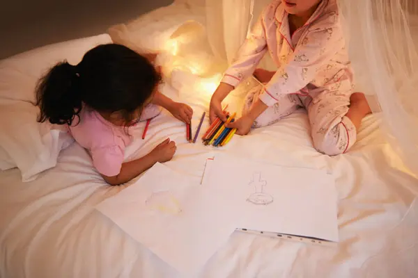女孩们 用彩色铅笔和画在床上过夜 周末在卧室里创作和放松 年幼的孩子 晚上穿着睡衣玩或教育玩具 或在家里被仙女的光芒连在一起 — 图库照片