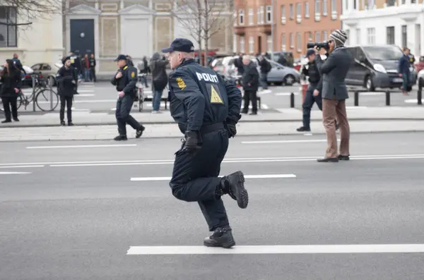 Police officer, man and running in street with crowd safety with protection service for public in city. People, law enforcement and justice in danger, arrest or warning on urban road in Copenhagen.