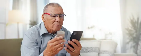 Phone, medicine and senior man with home research, reading label and learning of telehealth services. Online patient with pills bottle, tablet and mobile for information or health benefits on a sofa.