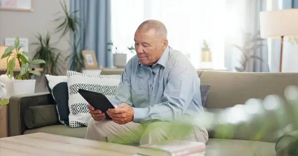 平板电脑 家里和老年人在沙发上 在客厅里看电子邮件或电子书放松一下 科技和老年人在休息室里做填字游戏 新闻和网络应用信息 — 图库照片