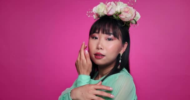 スキンケアのための花冠を持つアジアの女性のピンクの背景 美しさと顔 スタジオで自然と化粧品のための人のサロン 花の美学と肖像 — ストック動画