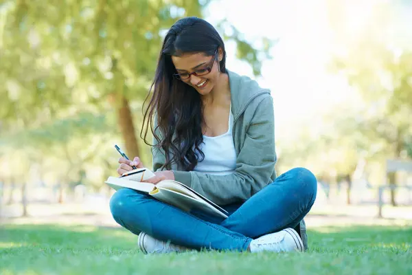 Writing, grass or happy woman in nature with notes for learning knowledge, information or education. Smile, diary journal or student in park for studying idea or peace on college campus lawn to relax.