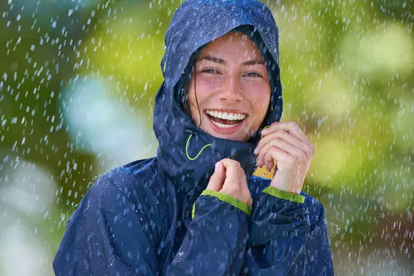 Woman, rain and portrait with laughing from winter climate, water and weather outdoor in a park. Happy, travel and female person with jacket for cold on holiday and vacation with raincoat and joy.