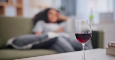 Kadın, cam ve şarap oturma odasında, düşünceli, yorgun ve akşamdan kalma haliyle. Kadın kişi, baş ağrısı ve madde bağımlılığı baskısı, alkol ve zihinsel sağlık sorunları.