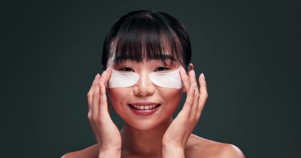 レチノール製品 フェイシャル 美容ルーチンでスタジオでアジア女性のスキンケア アイパッド 暗い緑の背景の皮膚科のためのコラーゲンのパッチが付いている笑顔 化粧品の利点および少女 — ストック動画